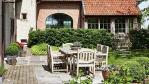 A brick building with a tiled roof, a wooden table and chairs, and a garden with various plants. - Country House in Sint Laureins Near Het Zwin (Sint-Laureins)