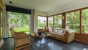 A spacious living room with a large window, a sofa, a coffee table, and a wicker chair. - Country House in Sint Laureins Near Het Zwin (Sint-Laureins)