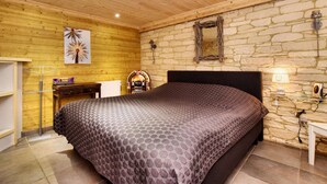Une chambre à coucher avec un lit, un plafond en bois, un mur en pierre et un petit bureau avec une lampe.
