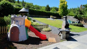 Une aire de jeux avec une structure ludique sur le thème d’un château, un toboggan et un barbecue.