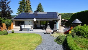 Une maison dotée d’un toit équipé de panneaux solaires, d’un espace barbecue et d’un jardin bien entretenu.