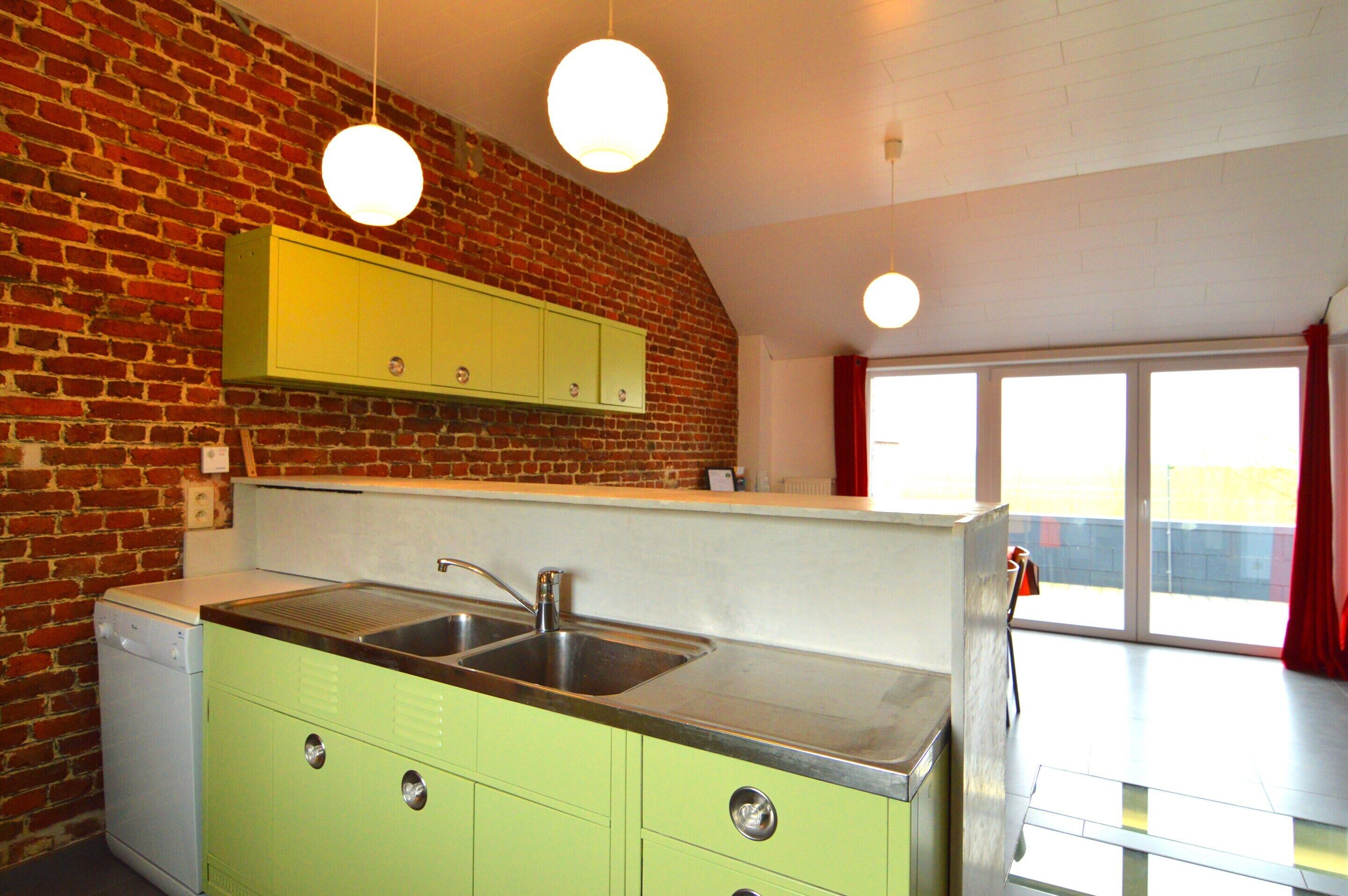A kitchen with a brick wall, a stainless steel sink, and green cabinets.