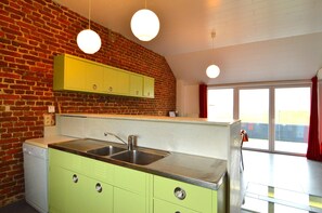 Una cocina con pared de ladrillo, un lavamanos de acero inoxidable y armarios verdes.