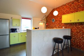 A kitchen with a brick wall, a refrigerator, a microwave, and a yellow cabinet.