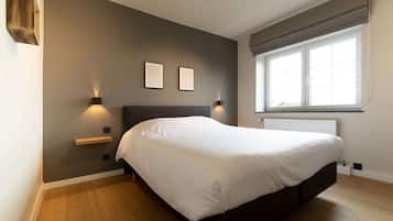 A bedroom with a large bed, two wall-mounted lights, a window with blinds, and a radiator.