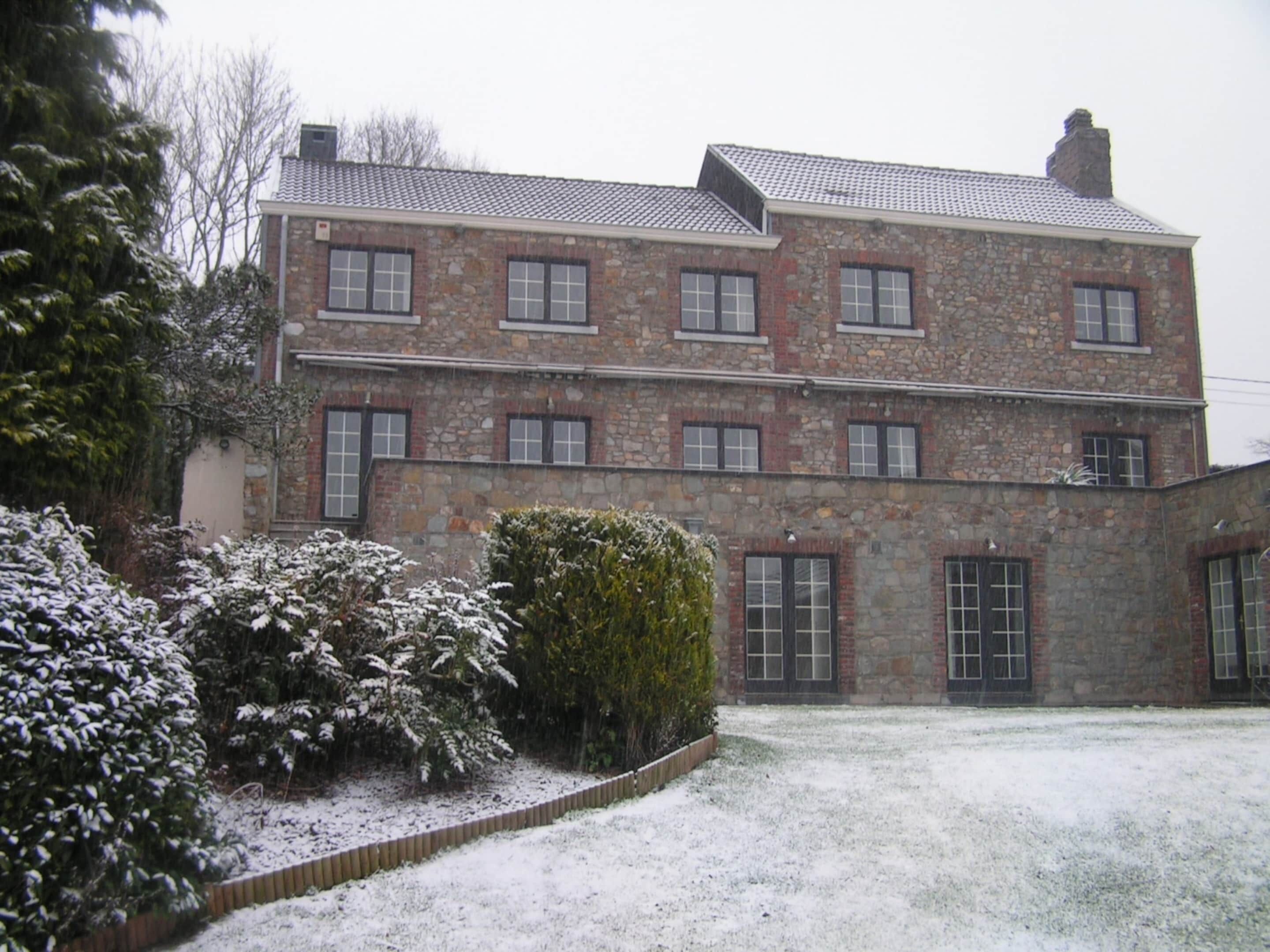 Un edificio de piedra de dos pisos con múltiples ventanas y un césped cubierto de nieve.