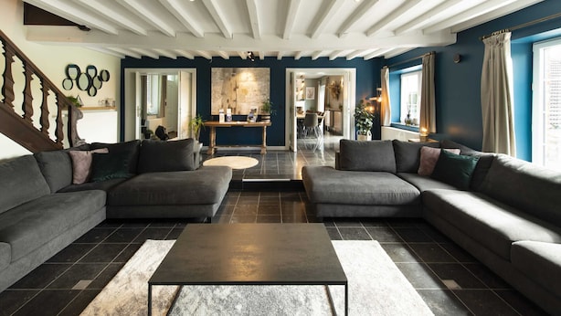 A modern living room with dark sofas, a central coffee table, and a staircase with decorative railings. - Modern House With Private Pool in Aubel (Aubel)