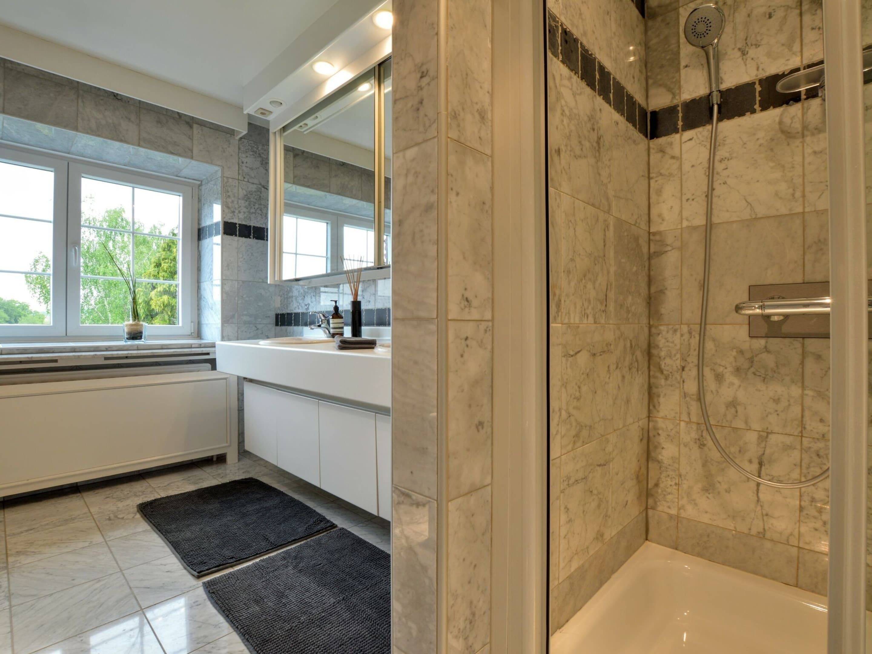 Un baño moderno con cabina de ducha, un espejo grande y una ventana que proporciona luz natural.