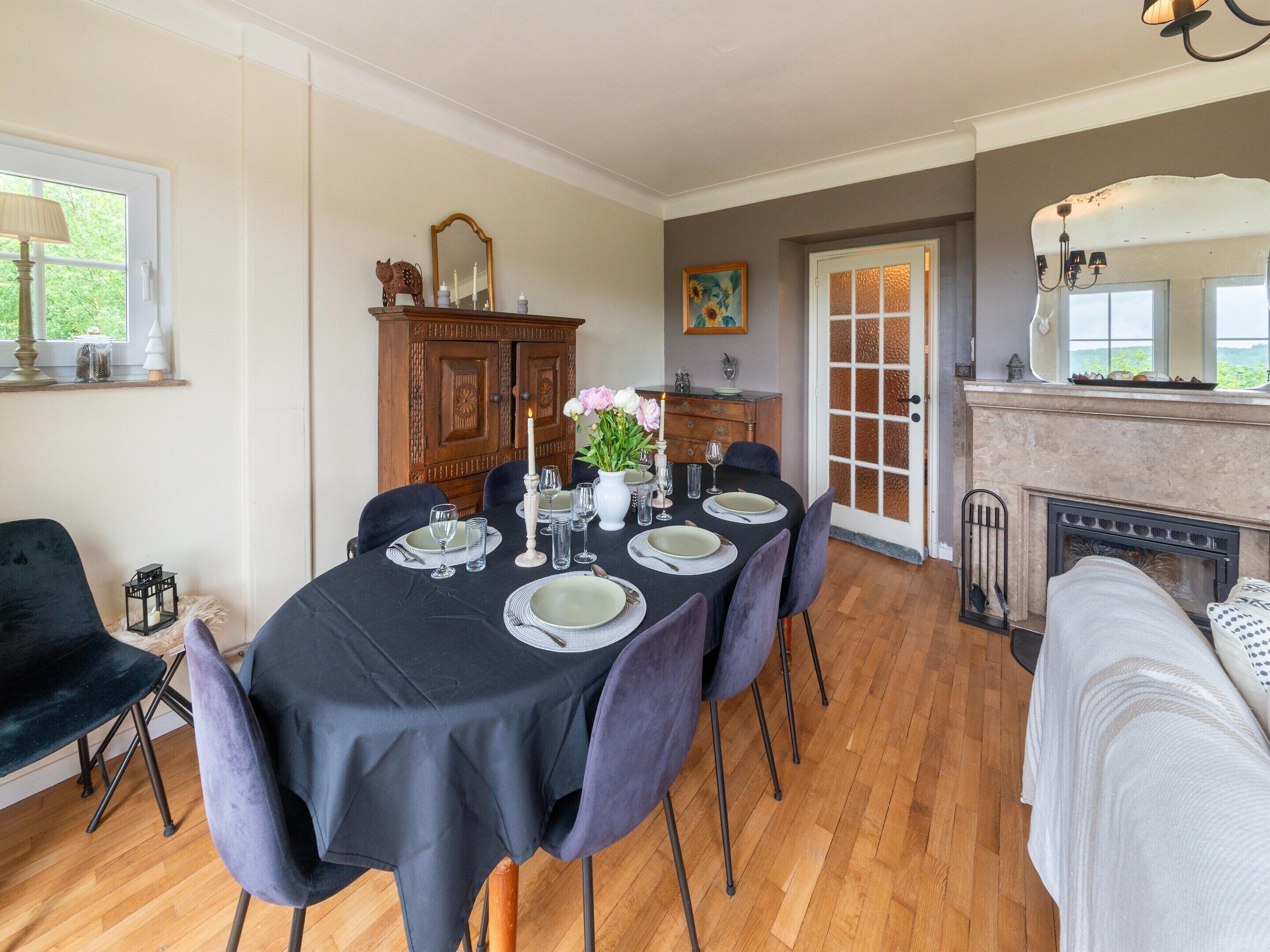 A dining room with a table set for six, a fireplace, and a large mirror above the mantel.