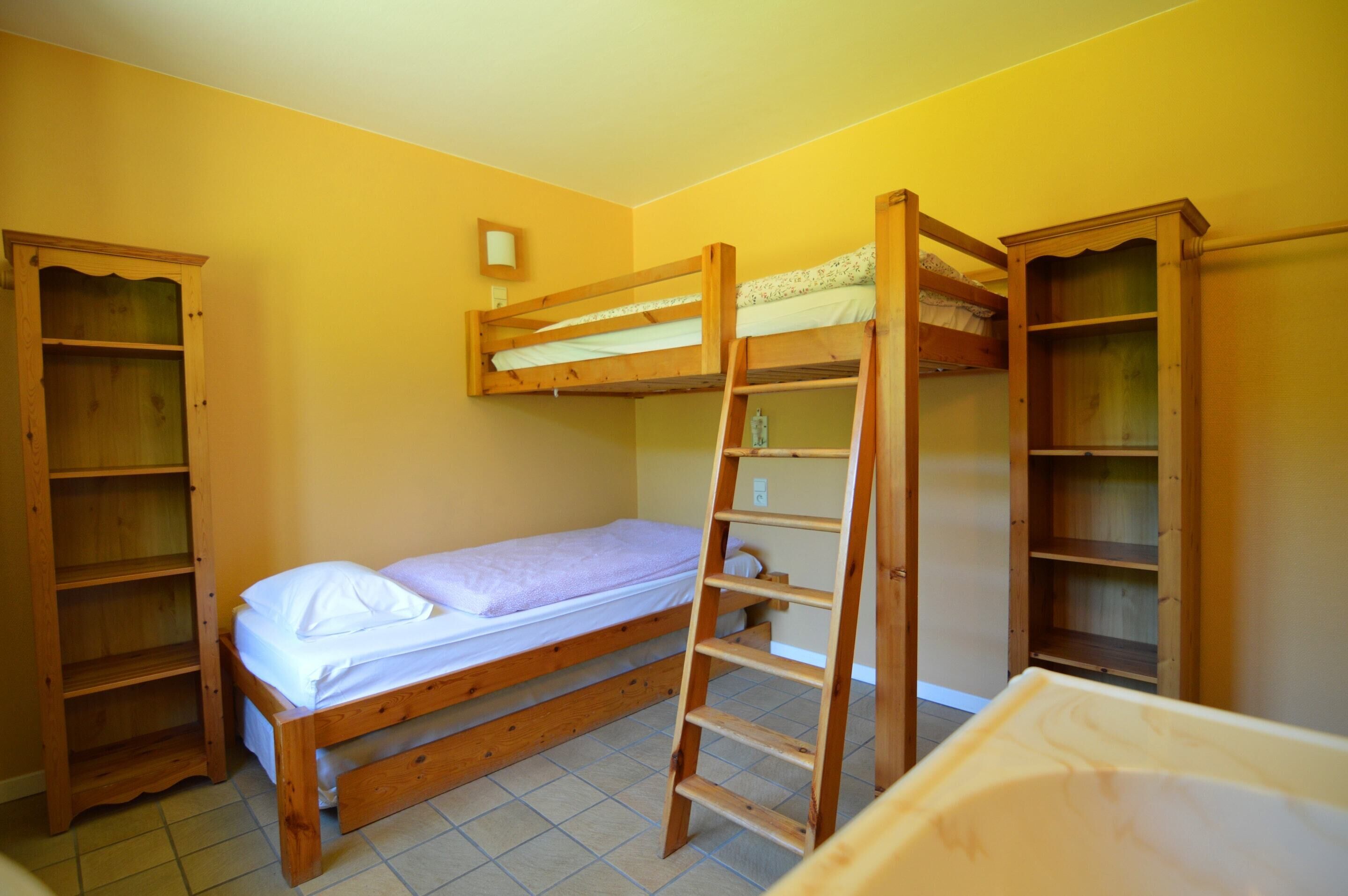 Quarto com beliche, escada, prateleiras de madeira e pequeno apoio acima da cama.