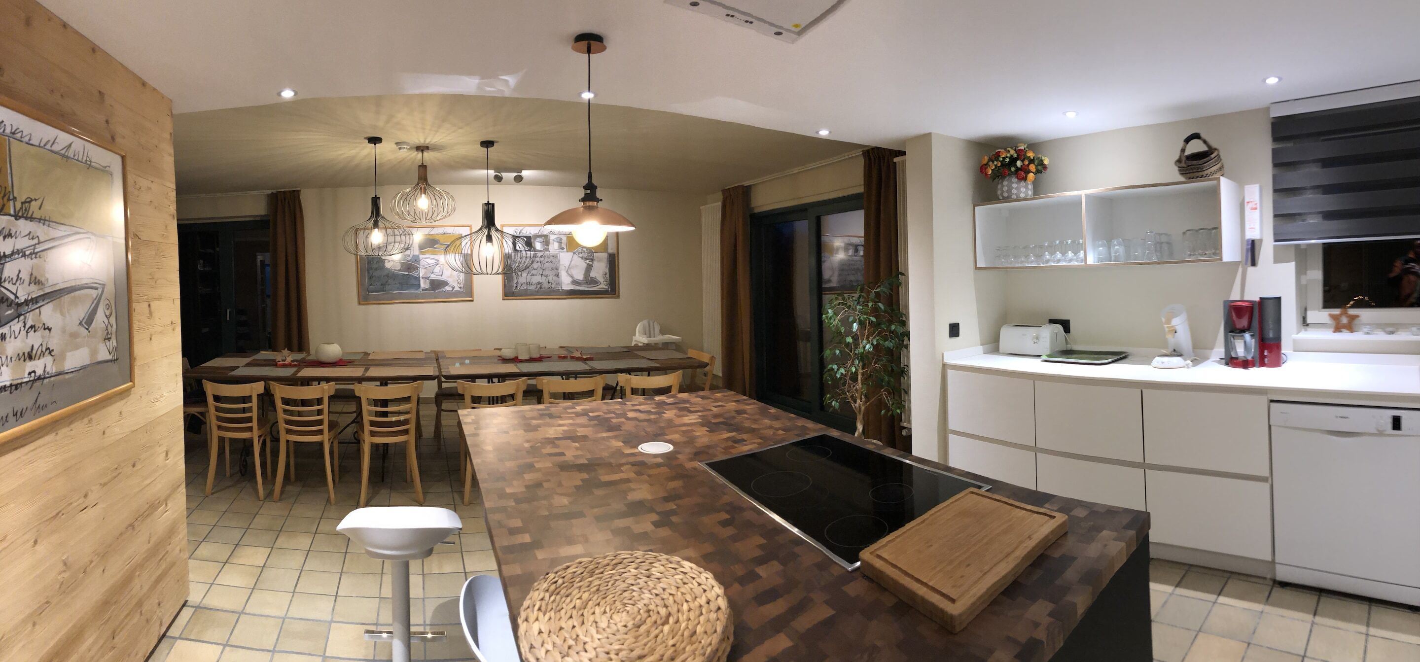 A modern kitchen with a central island, pendant lighting, and a dining area with wooden chairs.