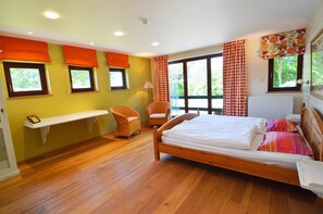 Une chambre à coucher avec un lit en bois, deux chaises, une étagère et de grandes fenêtres avec des rideaux.