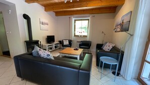 Een gezellige woonkamer met een zwarte bank, een houten salontafel en een televisie. Er is een open haard, een raam met gordijnen en een schilderij aan de muur.