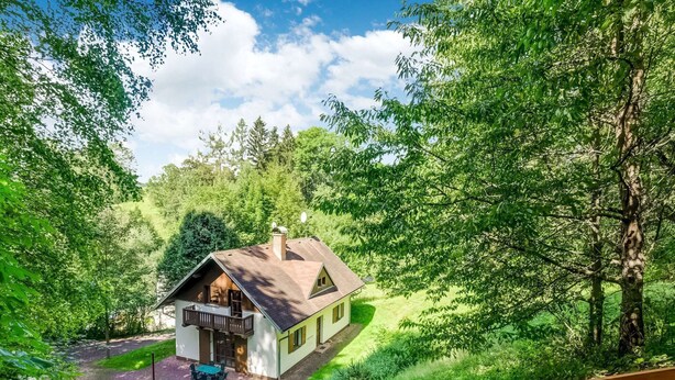 Een huis met balkon, omgeven door weelderige begroeiing en bomen.