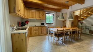 Een keuken met houten kastjes, een eettafel met stoelen, een raam en een trap.