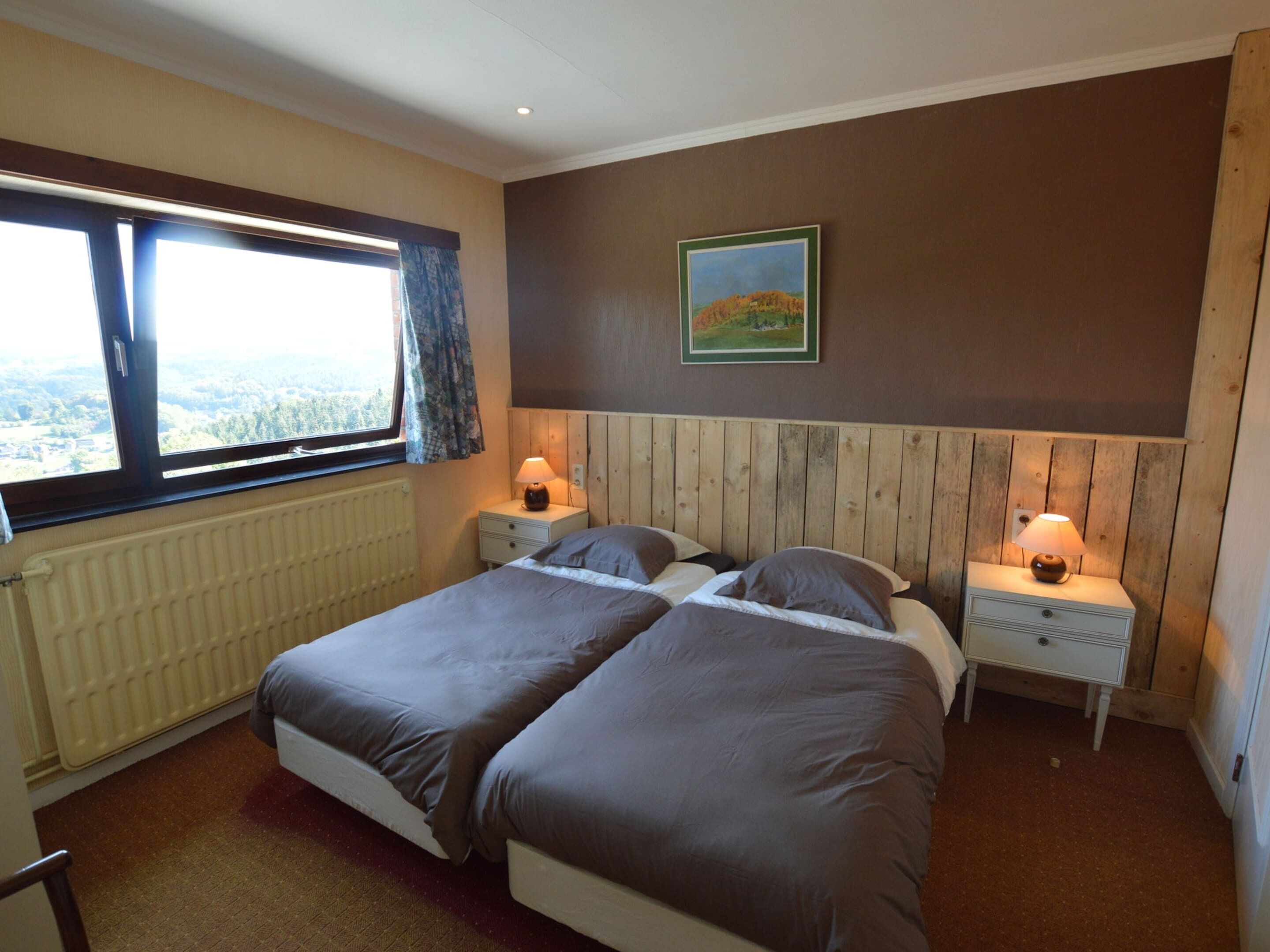 A bedroom with two beds, a window with a view, a painting on the wall, and a radiator.