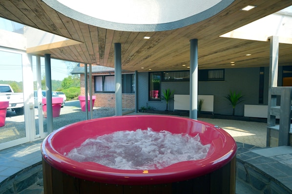 A hot tub in a covered outdoor area with a view of parked cars and a building in the background.