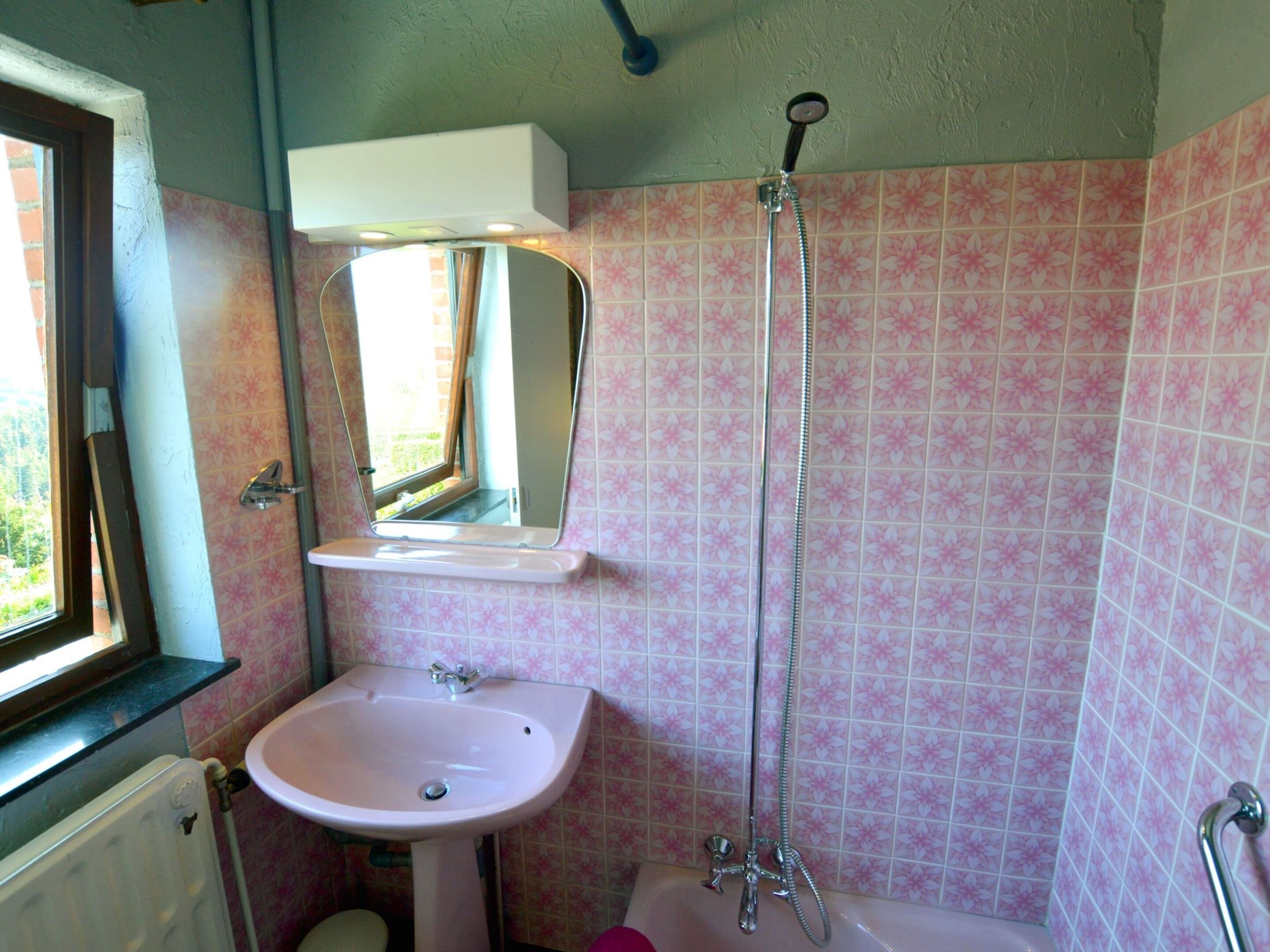 A bathroom with a sink, mirror, shower, and a window.