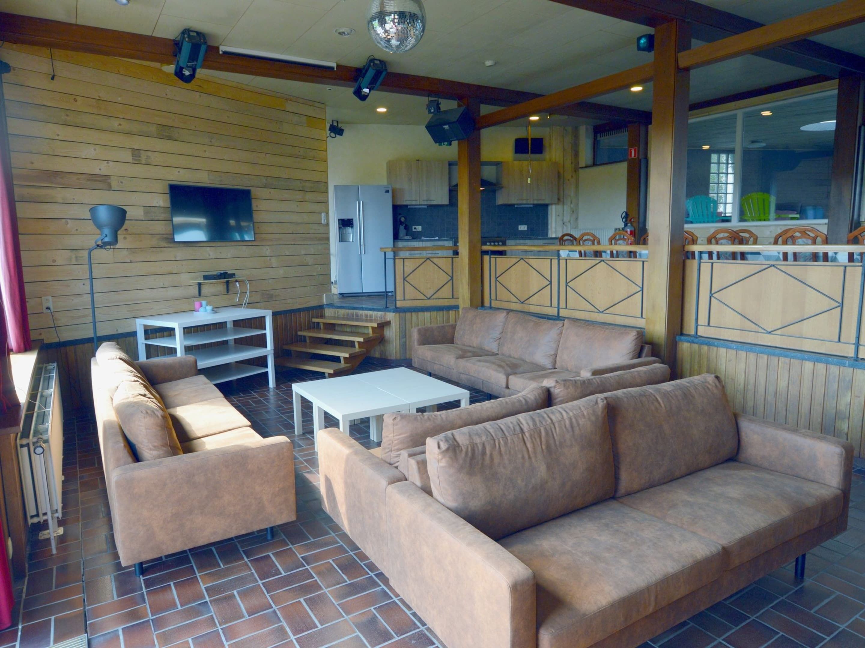 A spacious living area with a sofa set, a coffee table, and a TV. There is a kitchen area visible through a glass partition.