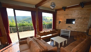 A spacious living room with a large sofa, a coffee table, and a TV mounted on a wooden wall. - Superb House for Family Group with Swimming Pool, Sauna, Hot Tub, Billiards (Trooz)