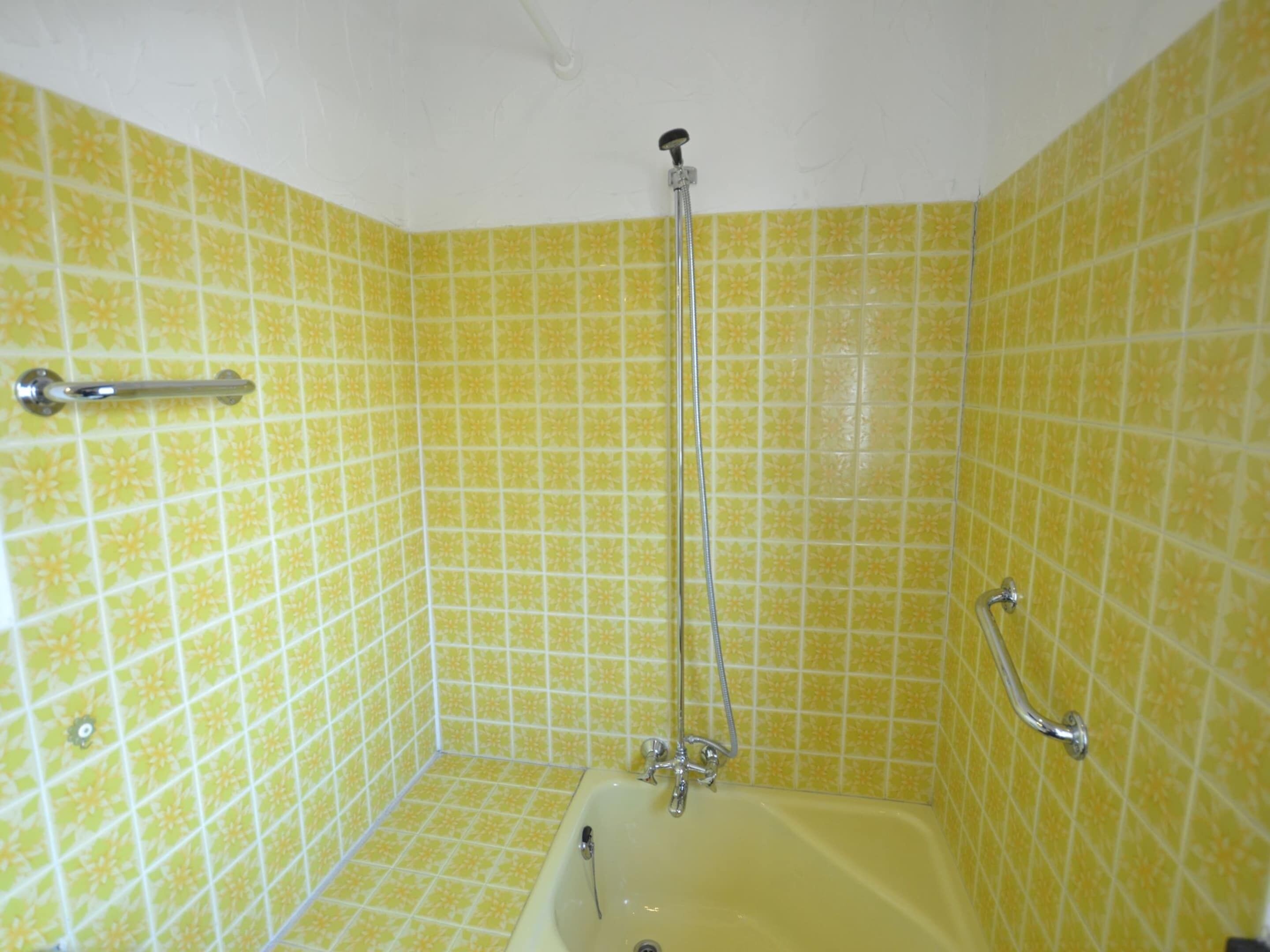 A bathroom with yellow patterned tiles, a bathtub, a showerhead, and a grab bar.