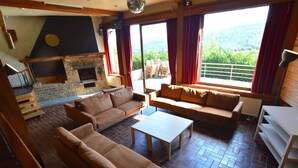 A cozy living room with a stone fireplace, a sofa, a coffee table, and a view of the outdoors. - Superb House for Family Group with Swimming Pool, Sauna, Hot Tub, Billiards (Trooz)