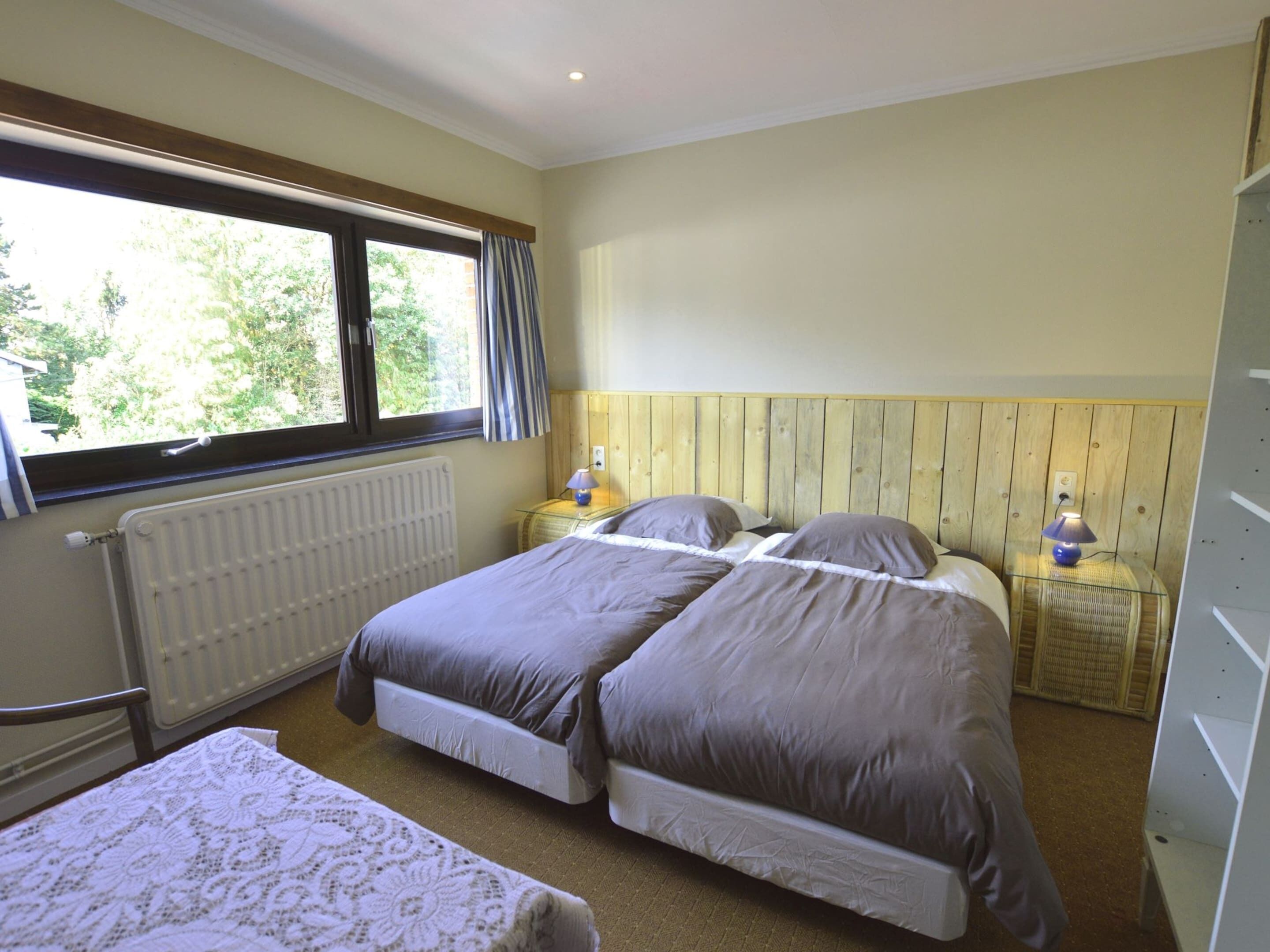 Une chambre avec deux lits, une fenêtre avec des rideaux, un radiateur et des lampes de chevet.