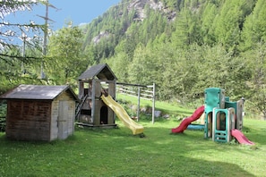 A playground with a slide and climbing structures, set against a backdrop of a forested hillside. - Chalet in Valais Near Ski Lift & Saas Valley (Saas-Balen)