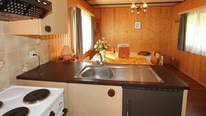 A kitchen with a stove, sink, and refrigerator. There is a dining table with a chair and a flower vase. - Chalet in Valais Near Ski Lift & Saas Valley (Saas-Balen)