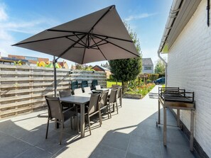 An outdoor patio with a table and chairs, a large umbrella, and a grill.