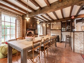 A rustic dining area with exposed wooden beams, a brick wall, and a large window with curtains.
