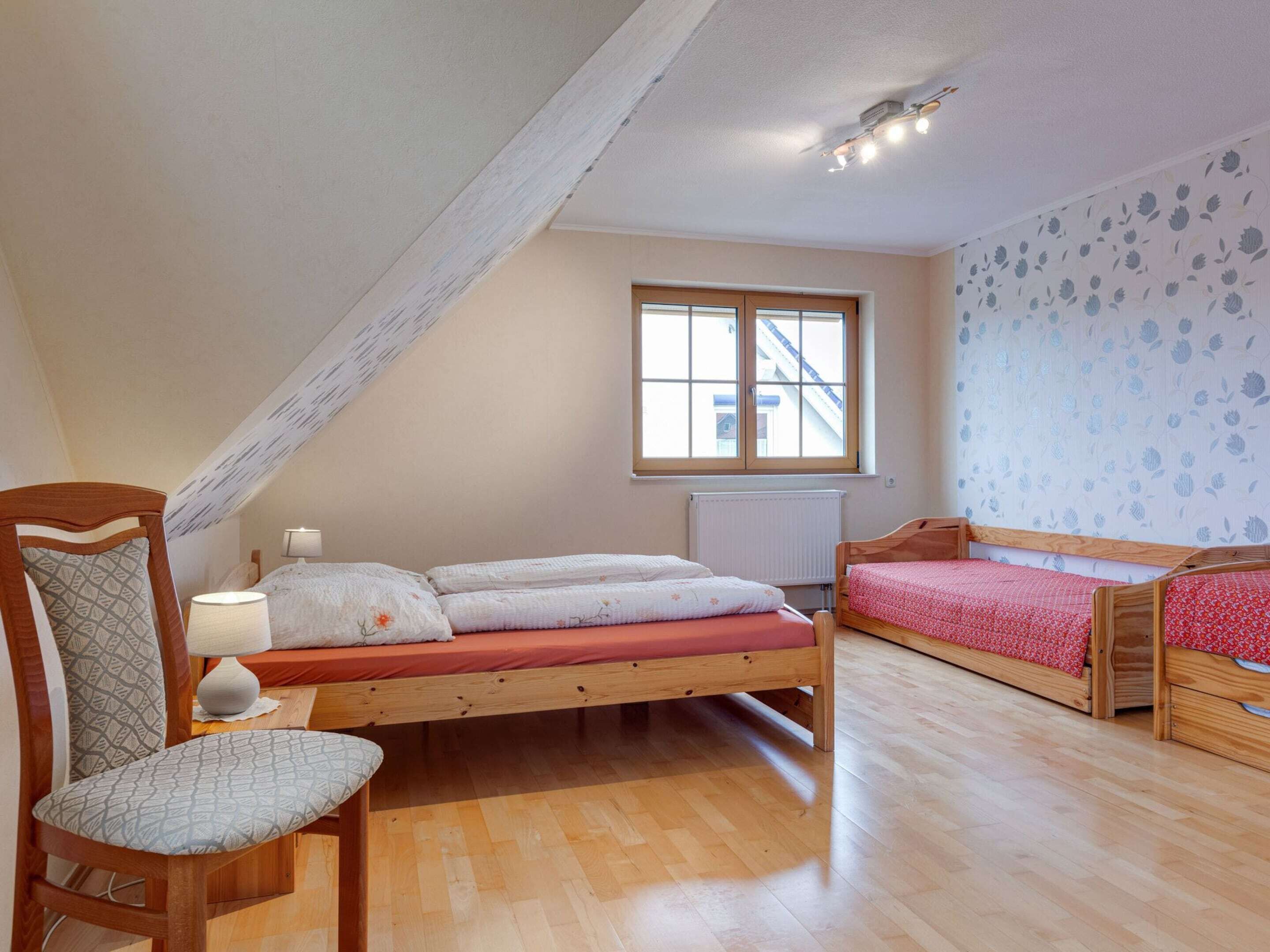 A cozy attic bedroom with a sloped ceiling, a large window, and a wooden floor.
