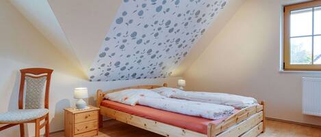 A bedroom with a sloped ceiling, a wooden bed, a chair, a nightstand, and a window.