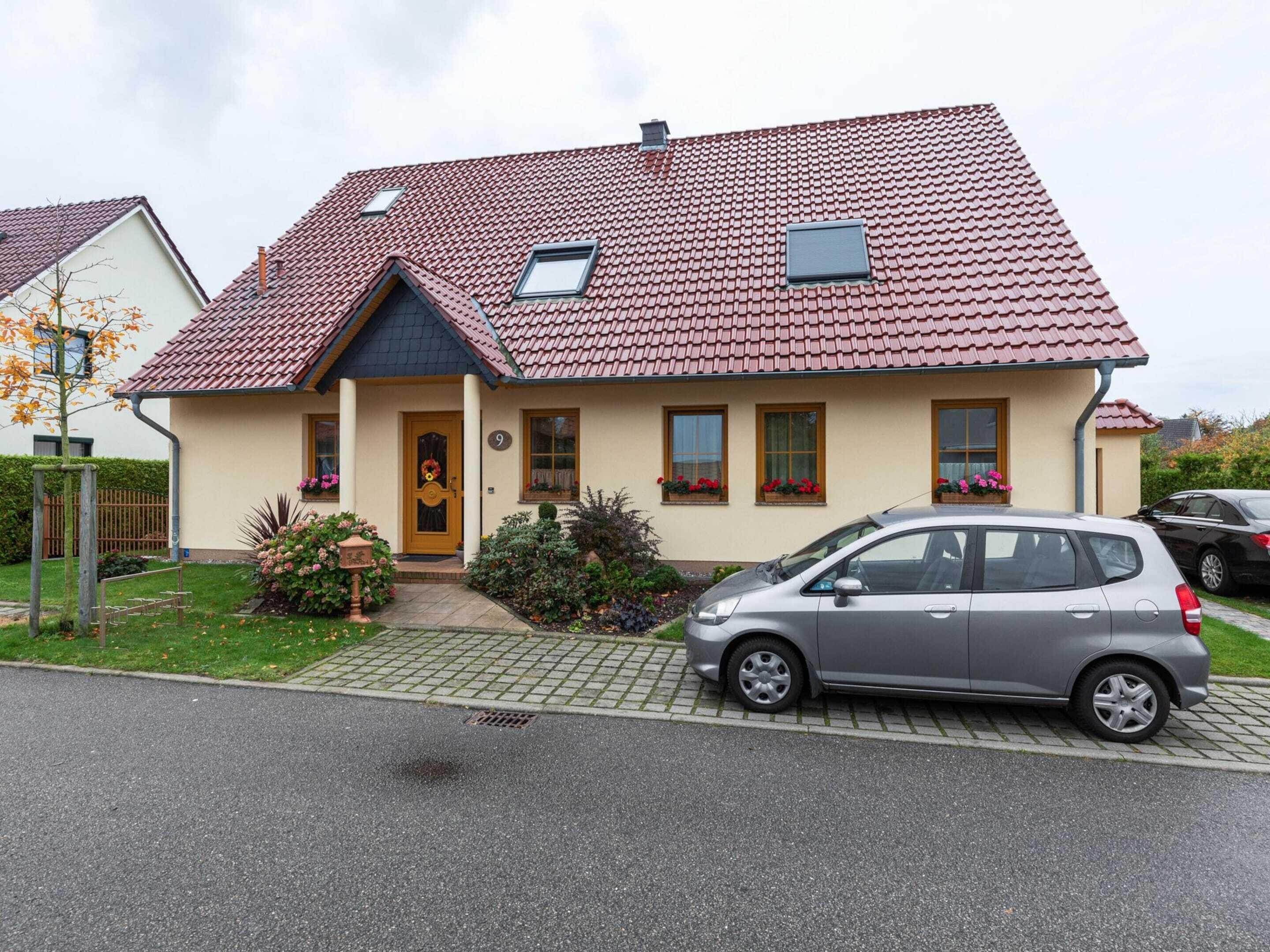 A two-story house with a red-tiled roof, a small attached garage, and a car parked in the driveway.