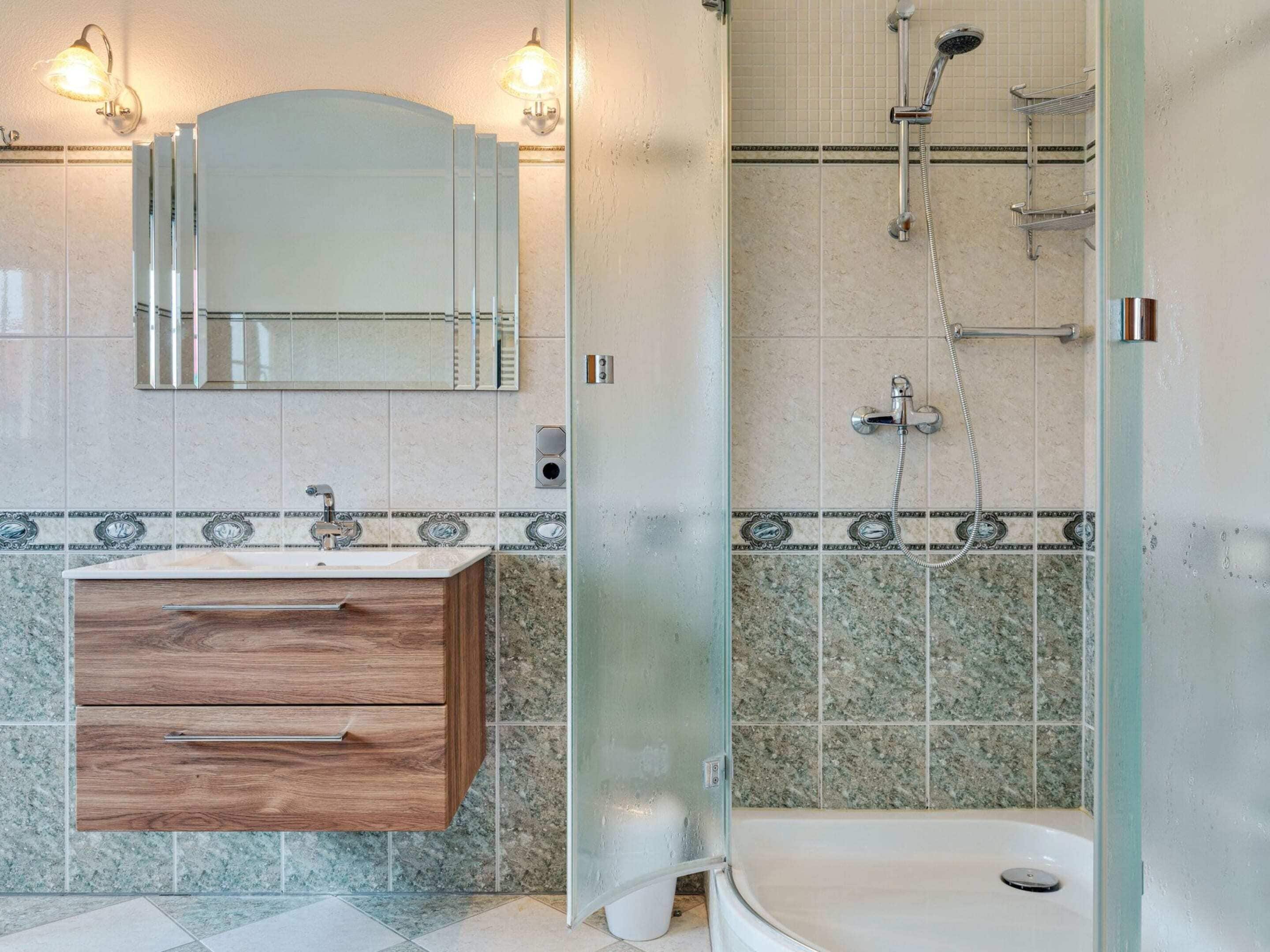 A bathroom with a wooden vanity, a glass shower enclosure, and a tiled backsplash.