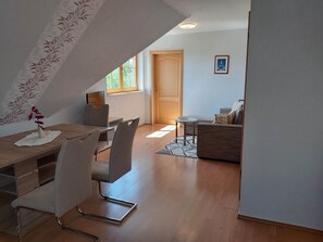 A modern living room with a dining area, featuring a wooden dining table, white chairs, a sofa, and a small side table. - Apartment in Kuhlungsborn Near Sandy Beach (Kuehlungsborn)