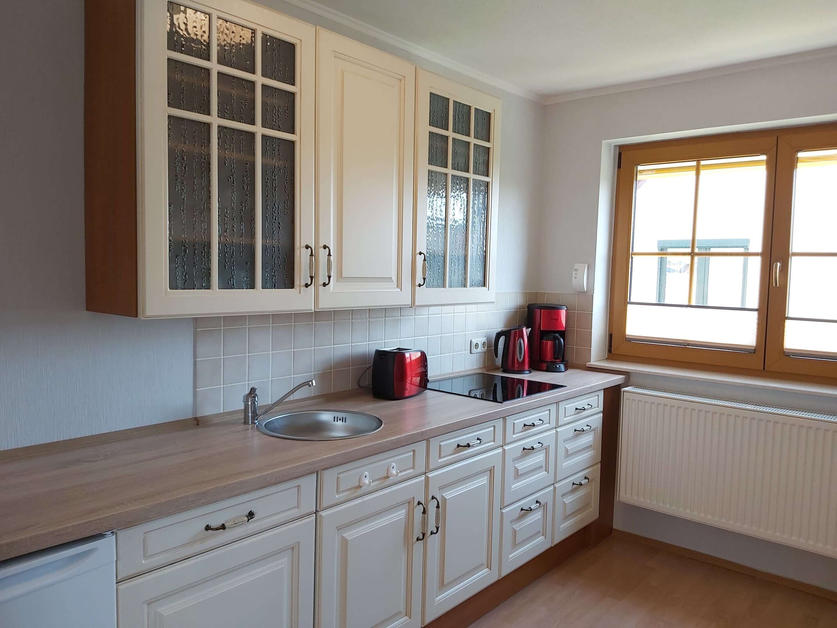A kitchen with white cabinets, a sink, a window, and a radiator.