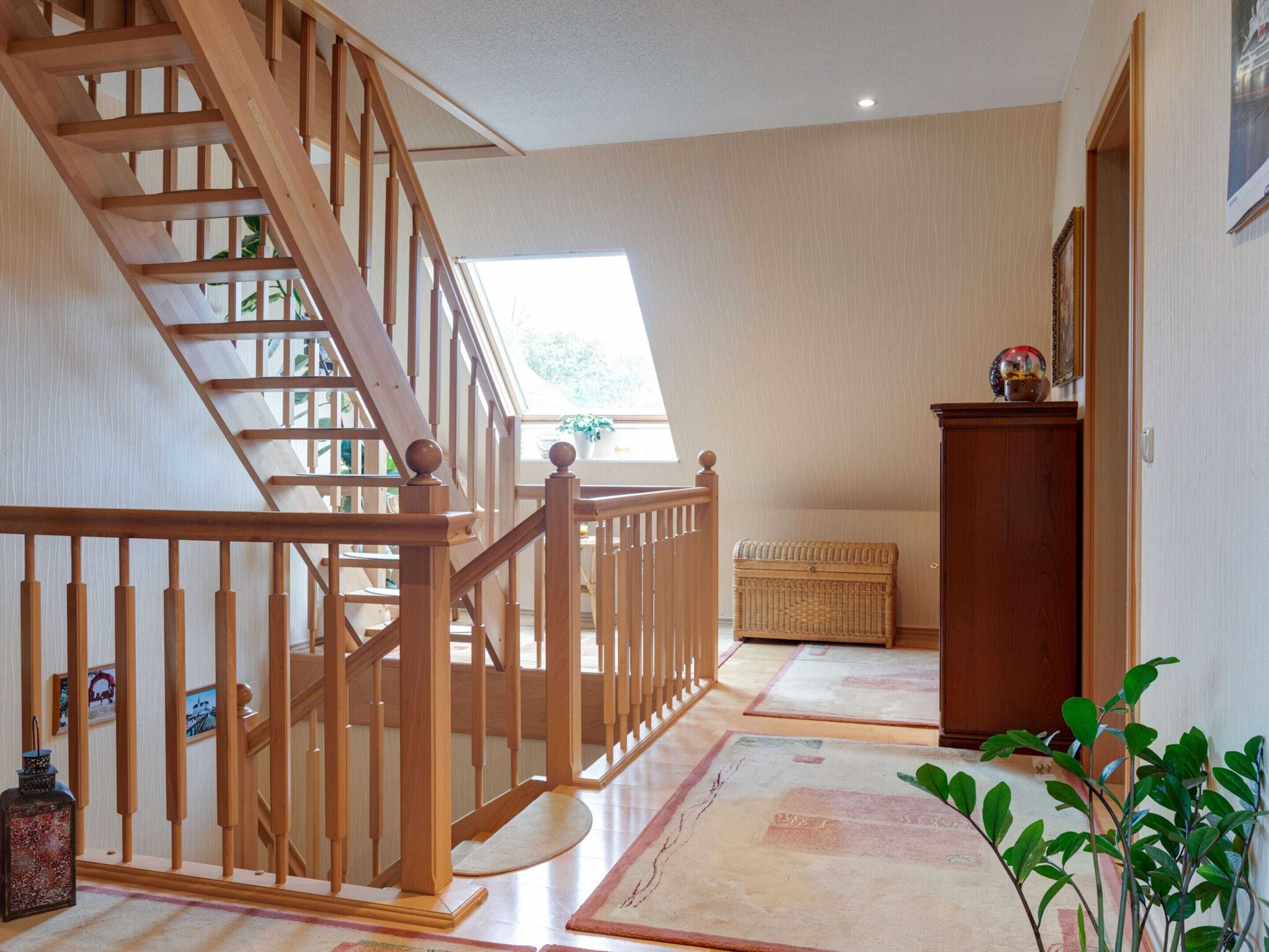 A wooden staircase leading to a loft bedroom with a skylight, a wicker chest, and a small cabinet.