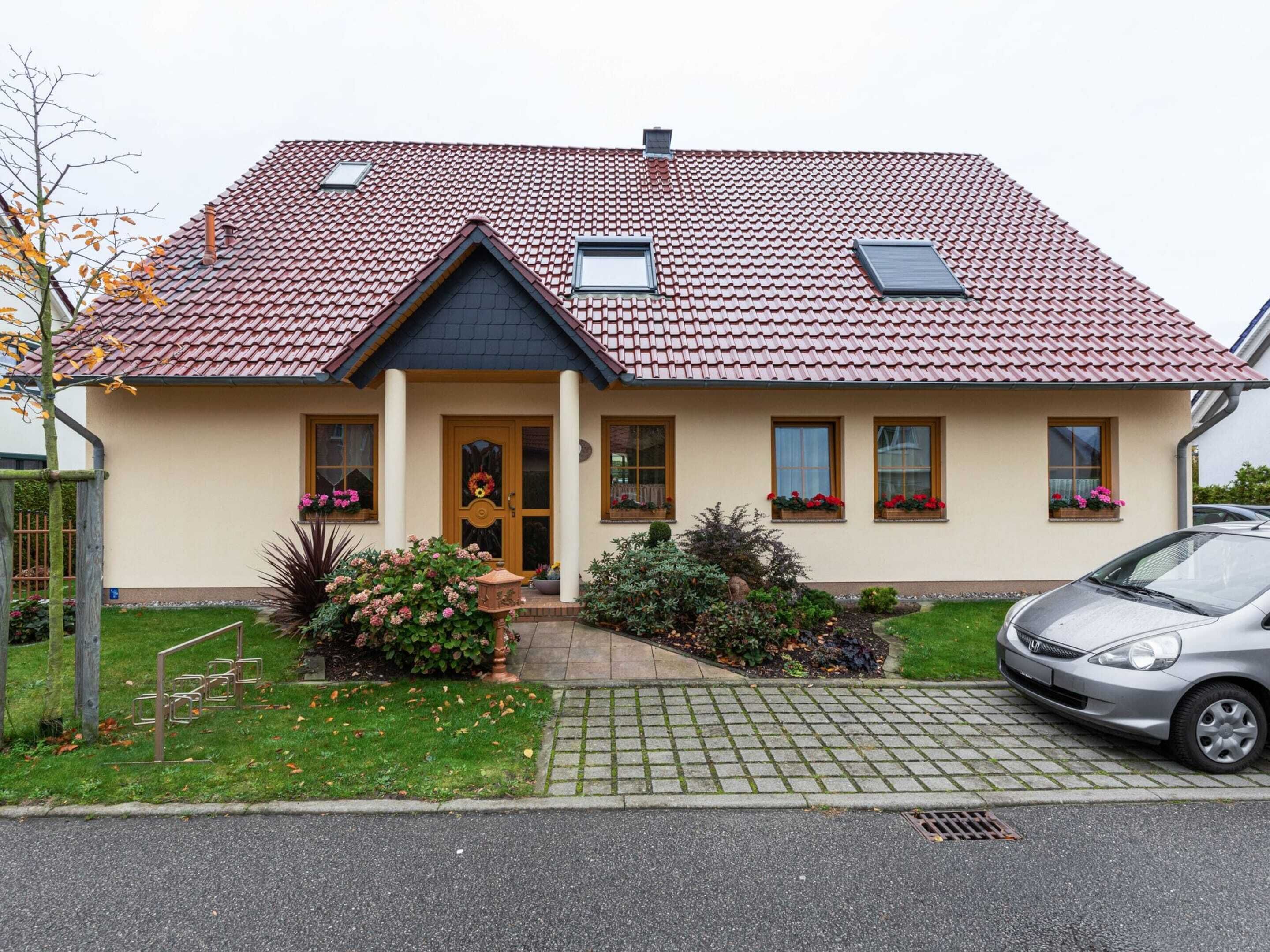 Ein zweistöckiges Haus mit Ziegeldach, einer Veranda und einem Auto auf der Auffahrt.
