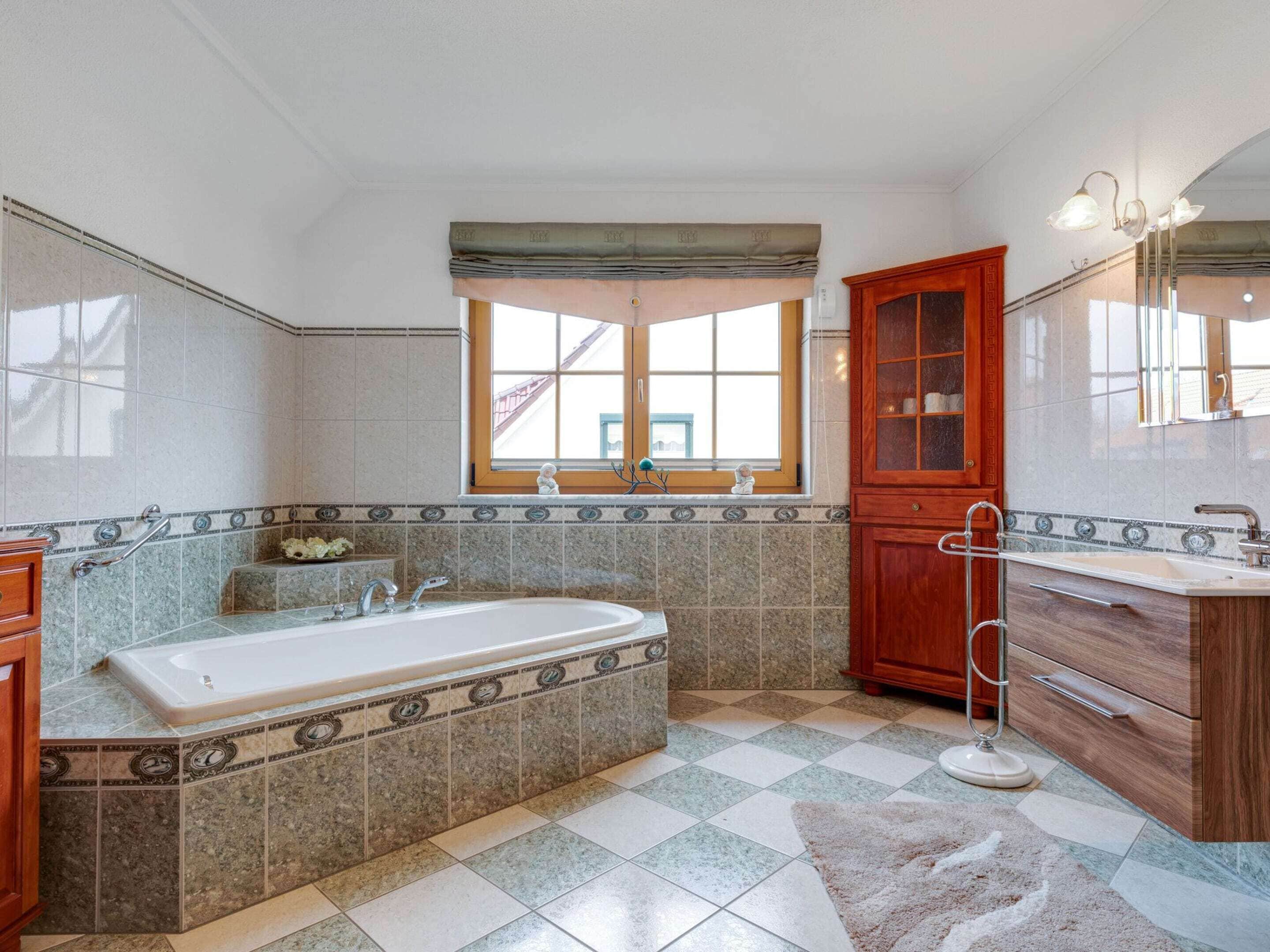A bathroom with a large bathtub, a wooden cabinet, and a tiled floor.