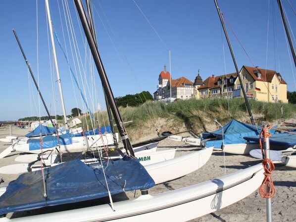 A beach with several sailboats docked, a sandy shore, and buildings in the background. - Apartment in Kuhlungsborn Near Sandy Beach (Kuehlungsborn)