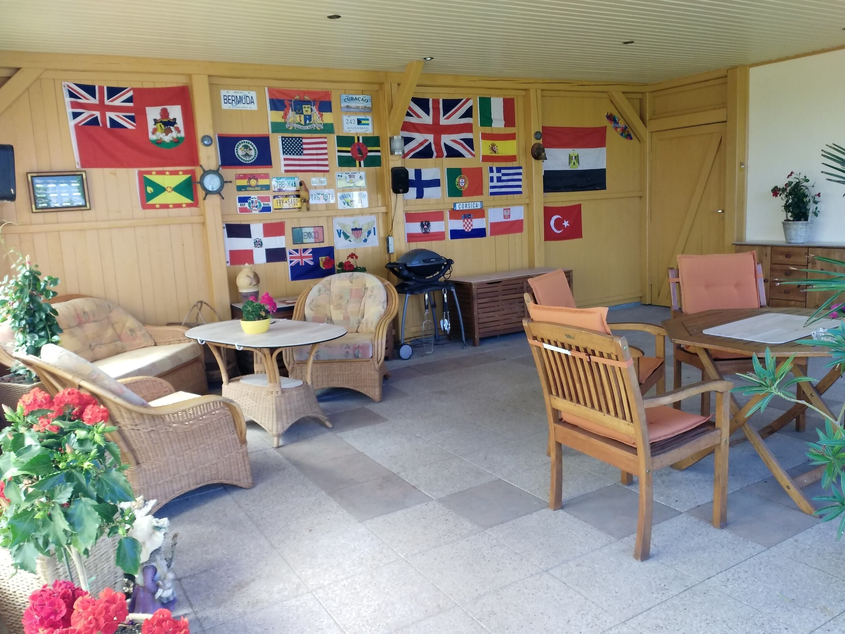 Una habitación con muebles de mimbre, una mesita y varias banderas en las paredes.