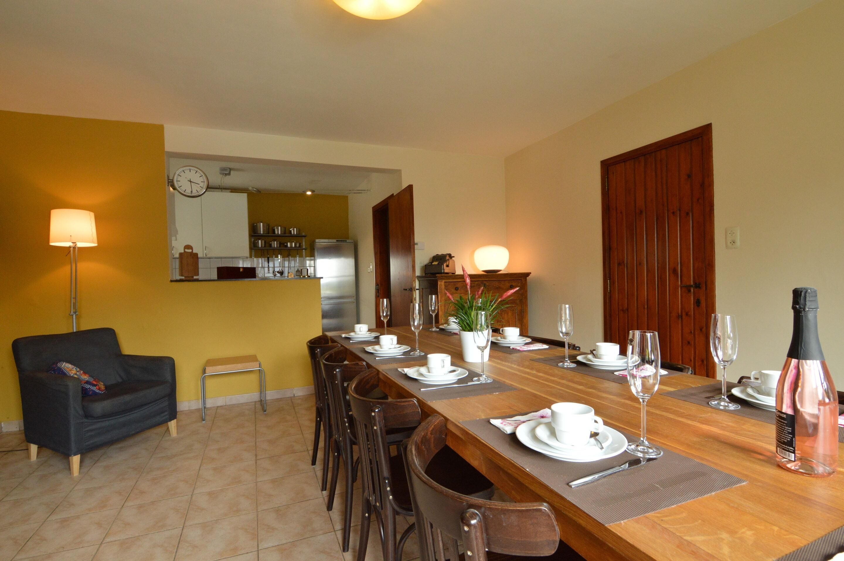 A dining area with a long table set for a meal, chairs, a sofa, a lamp, and a clock on the wall.