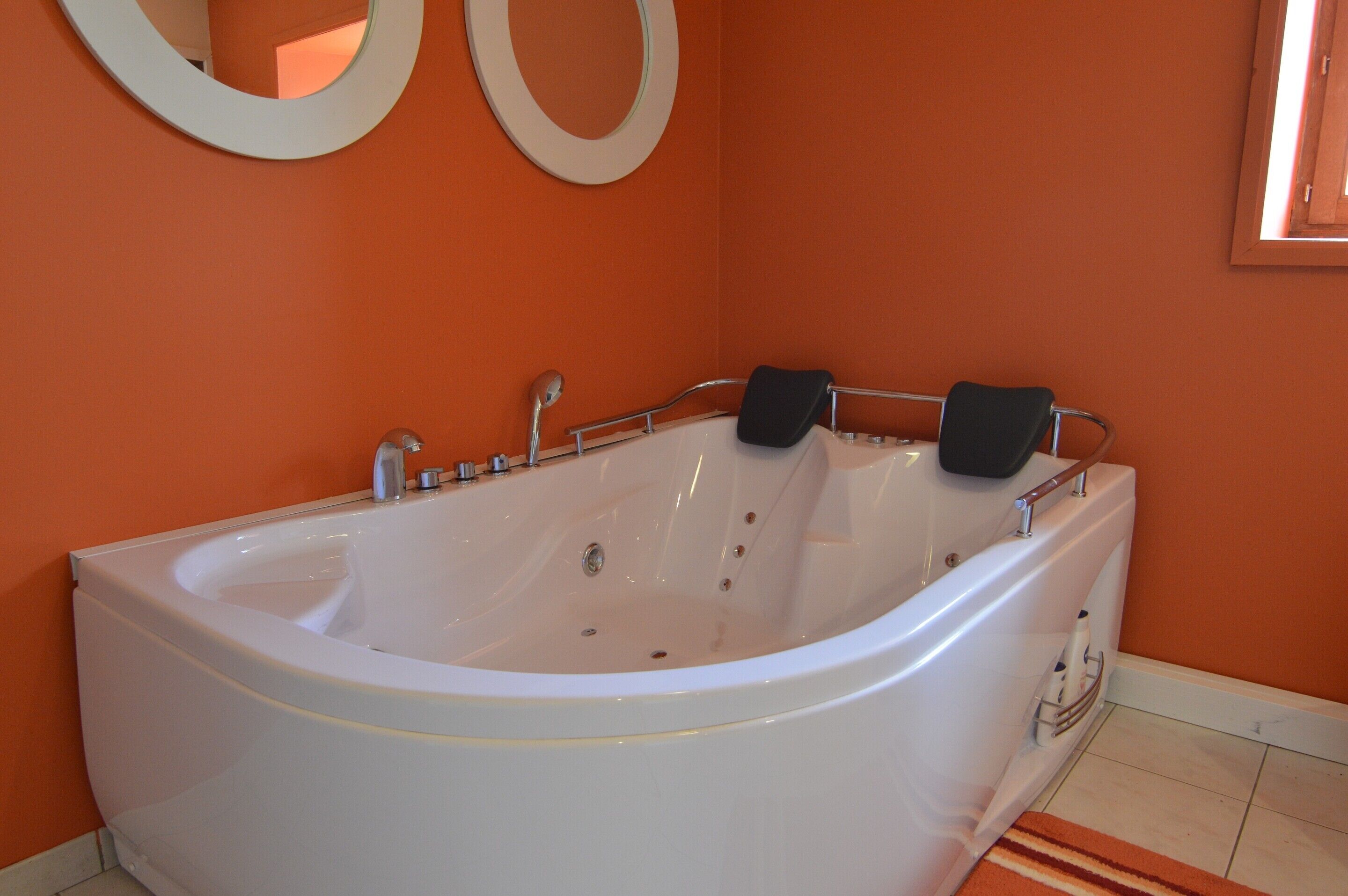 A large white bathtub in a bathroom with orange walls and a striped rug.