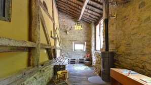 A rustic interior with stone walls, wooden beams, a fireplace, and a wooden rocking chair. - Holiday Home in Odeigne With Sauna (Manhay)