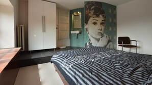 A bedroom with a bed, a chair, a wardrobe, a mirror, and a tiled wall with a mosaic. - Holiday Home in Odeigne With Sauna (Manhay)