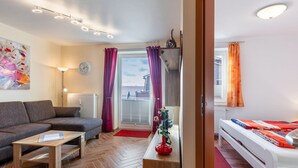 A modern living room with a sofa, coffee table, and a small table with a vase. There is a window with curtains, a radiator, and a clock on the wall. - Attractive Apartment in Boltenhagen near Sea (Boltenhagen)