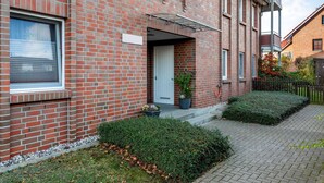 A red brick residential building with a white door, a small porch, and a potted plant. - Attractive Apartment in Boltenhagen near Sea (Boltenhagen)