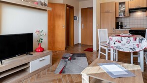 A modern living room with a flat-screen TV, a red vase with flowers, and a dining area with a table and chairs. - Attractive Apartment in Boltenhagen near Sea (Boltenhagen)