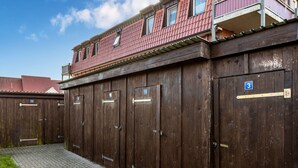 A row of wooden doors with numbered signs, a paved walkway, and a building with a red roof in the background. - Attractive Apartment in Boltenhagen near Sea (Boltenhagen)